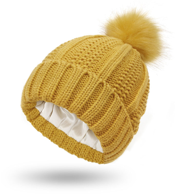 Satin-lined beanie with faux fur pom pom, yellow knit, wool material, stylish warmth for winter.