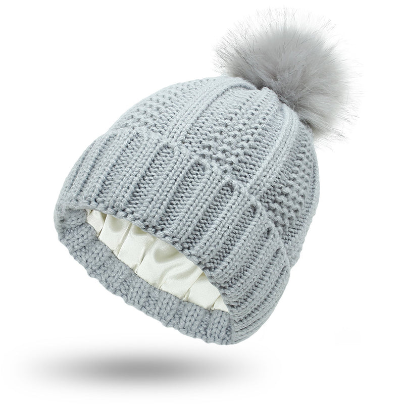 Satin-lined beanie with faux fur pom pom and knit texture, designed for warmth and hair protection.